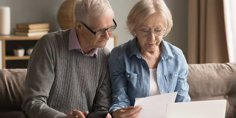Image of retired man and woman looking at paper bank statement with calculator and laptop