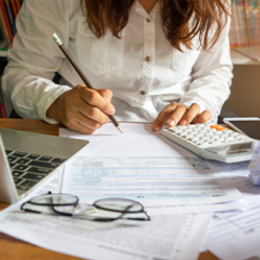 Person writing on top of financial document with calculator and laptop next to them