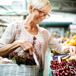 Senior woman smiling while picking fruits from stall to add to her basket at market