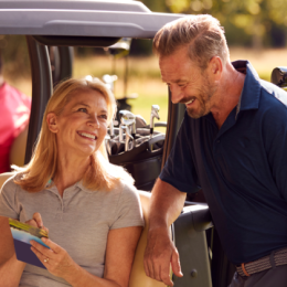 Image shows an older couple smiling together in front of a golf cart