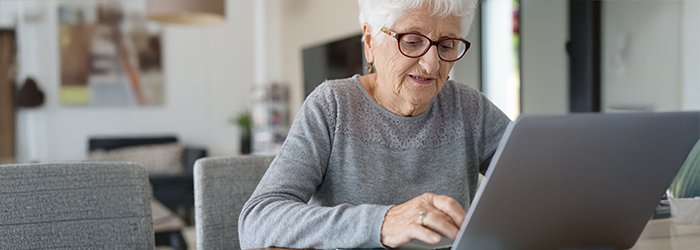 Senior woman with glasses on sitting at the table and typing on her laptop