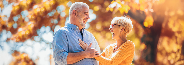Older man and woman smiling outdoors in fall setting