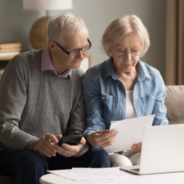 Image of retired man and woman looking at paper bank statement with calculator and laptop