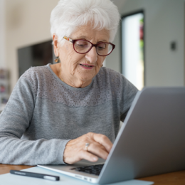 Senior woman with glasses on sitting at the table and typing on her laptop